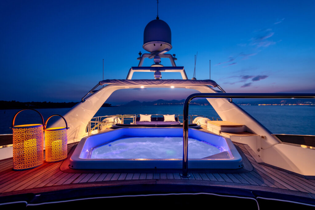 A luxury yacht with lights and a hot tub sailing in the sea at night