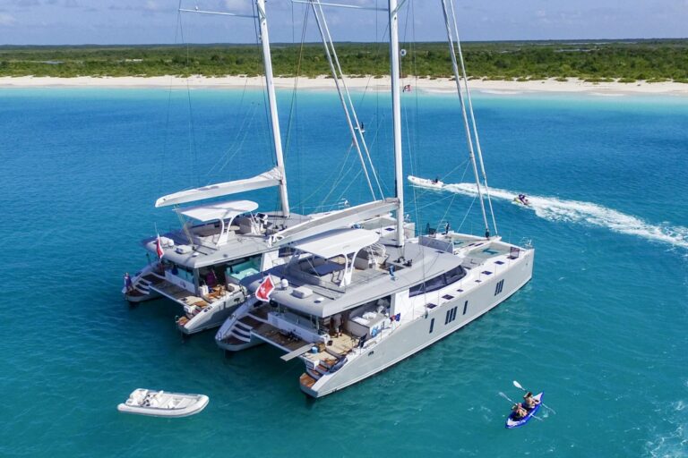 BVI Tandem Charters: 2 catamarans rafted up next to each other on anchor and people playing with water toys around them. Off white beach in the Caribbean