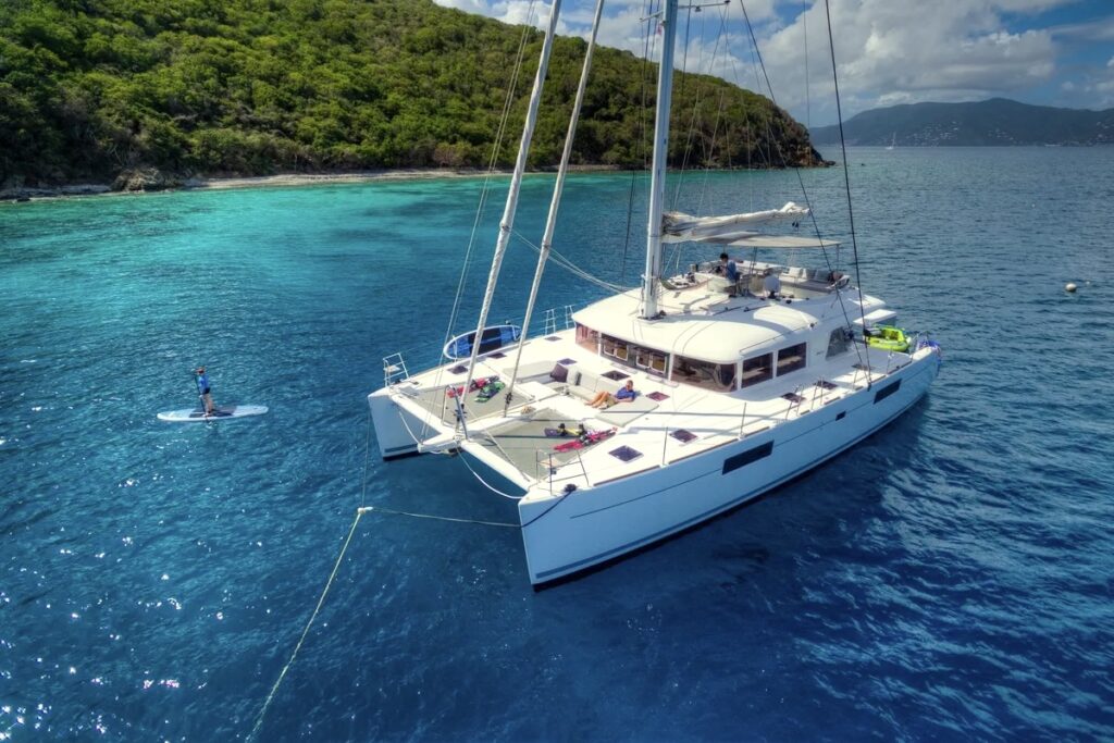 Crewed sailing catamaran at anchor in a calm BVI bay with a paddleboarder alongside