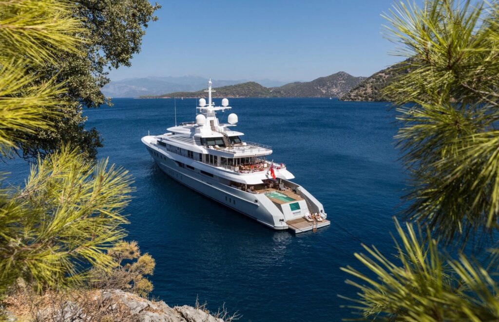 AXIOMA superyacht at anchor in a pine-lined bay