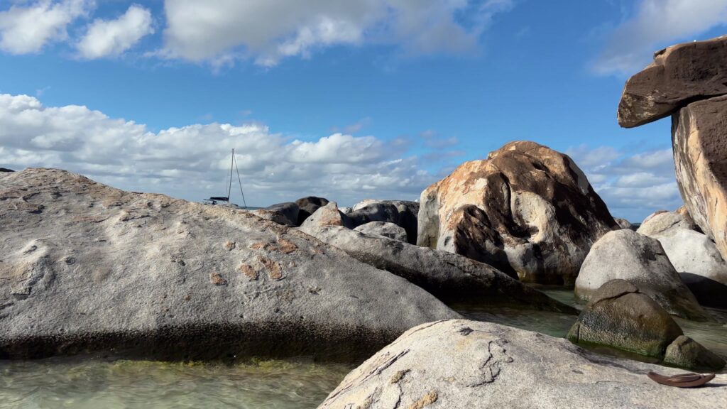 Tidal pools at The Baths with a yacht anchored beyond the rocks