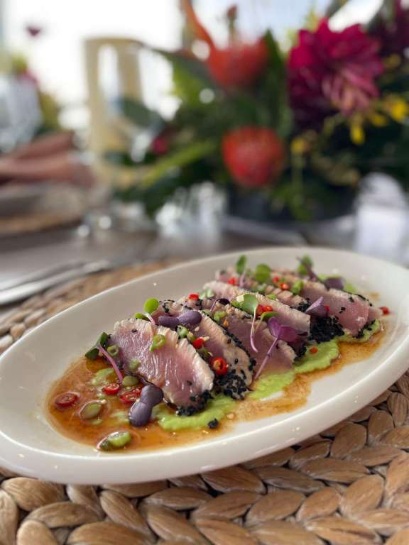 Amber's sesame-crusted seared tuna, thinly sliced and served atop a vibrant avocado purée. It's finished with a tangy soy-based sauce, garnished with microgreens, red chili slices, and black sesame seeds.