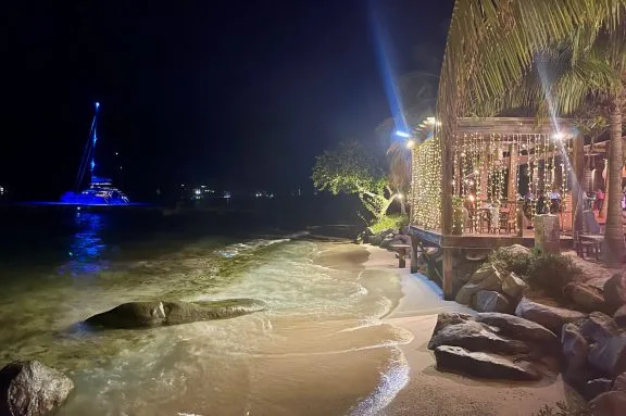 Catamaran lit up at night anchored in front of Coco Maya Beach Restaurant, Virgin Gorda