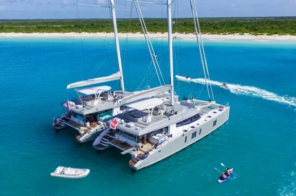 BVI Tandem Charters: 2 catamarans rafted up next to each other on anchor and people playing with water toys around them. Off white beach in the Caribbean
