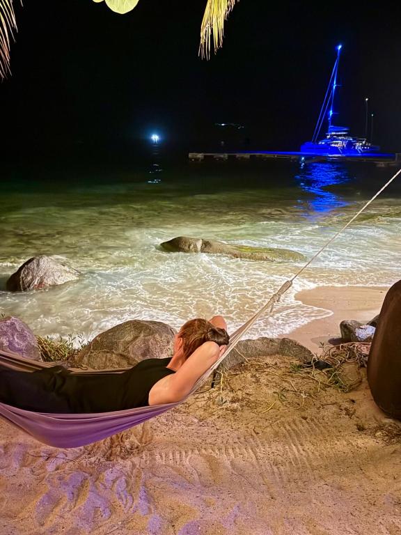 Woman in hammock on the beach at CocoMaya looking out at catamaran lighting up in the night, BVI